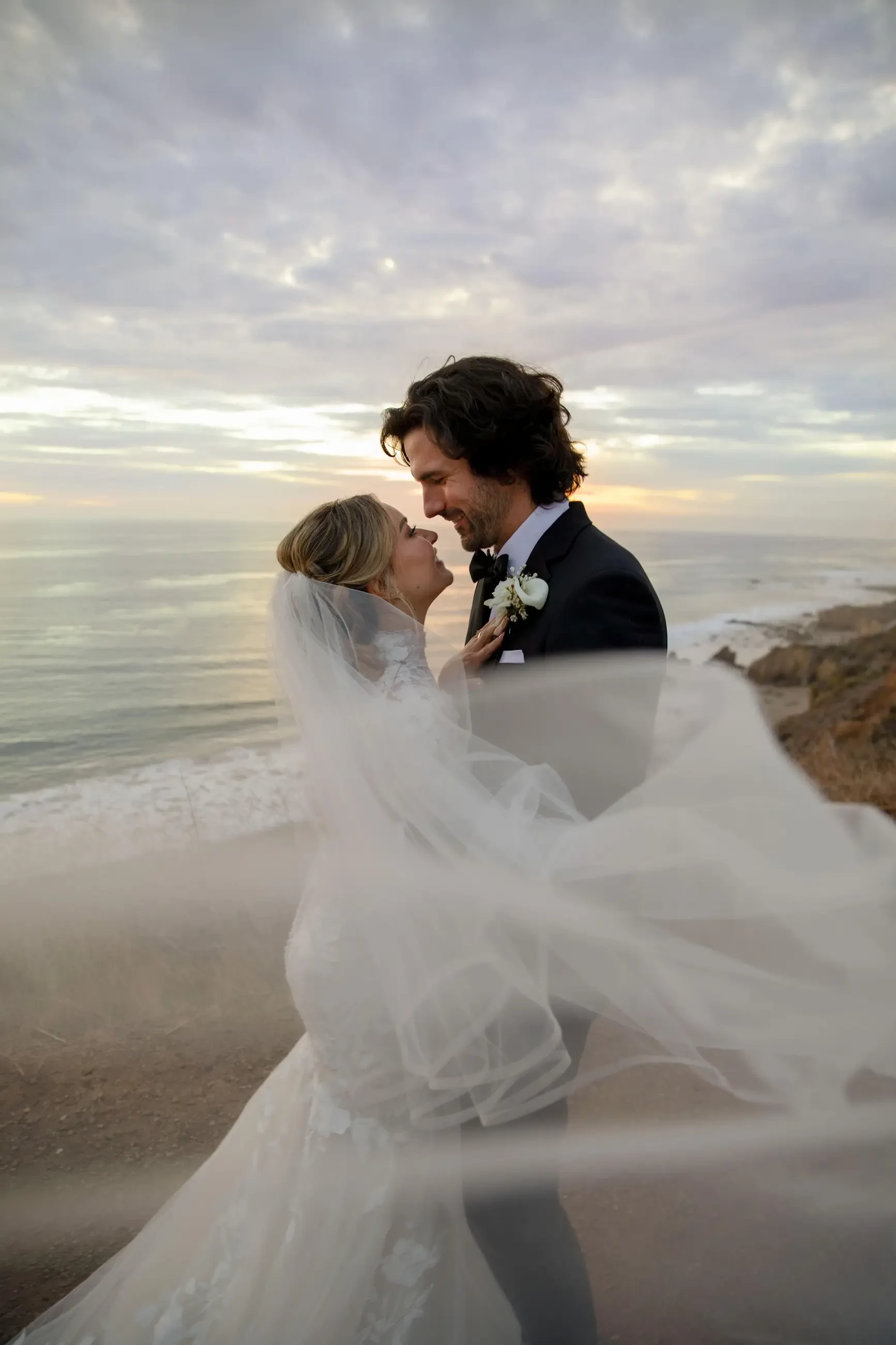 Сouple wearing a white gown and a black suit on the beach